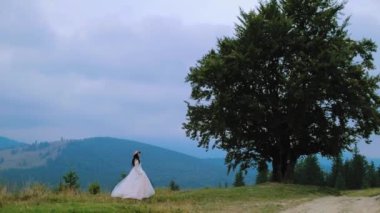 Dağlık alanda yürüyen güzel elbiseli gelin. Yazın dağlarda doğal manzara ve doğanın arasında beyaz gelinlikli bir kadın..