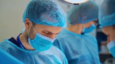 Mavi maskeli doktorun portresi aşağıya bakıyor. Ameliyathanede deneyimli cerrahlar hastanın hayatını kurtarıyor. Yakın plan..