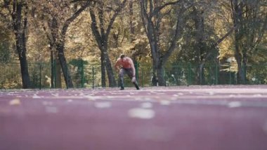 Stadyumda sağlıklı bir atlet koşuyor. Genç sporcu, sonbahar ağaçlarının arka planında koşuya katılıyor. Aşağıdan görüntüle.