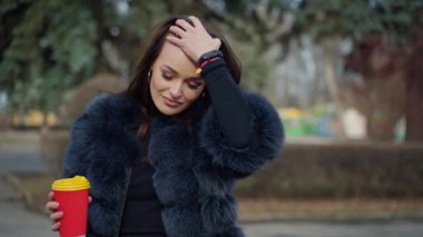 Açık havada sosyetik bir kızın portresi. Parkta bir fincan kahveyle kameraya poz veren güzel görünümlü esmer manken. Yavaş çekim.