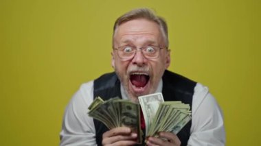 Dolarlar sallayan heyecanlı olgun bir adam. Mutlu, komik, yaşlı iş adamı kameraya ağzını açarak banknotlar gösteriyor. Pozitif duygular.