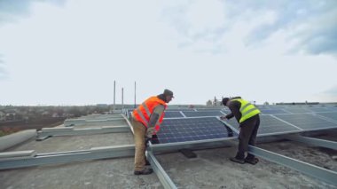 Çatıya güneşli piller yerleştirildi. Üniformalı iki işçi güneş çiftliğine metal bazlı fotovoltaik paneller kuruyor..