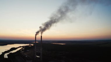 Ekolojik felaket. Akşamları endüstriyel borulardan gelen kirli emisyonlar doğal çevreye yayılıyor. Gün batımında nehrin yanındaki fabrikada..