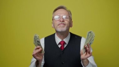 Dolarları olan gri saçlı bir adamın portresi. Gözlüklü, gülümseyen, para saçan ve mutlu mesut yüzüne dokunan yetişkin bir iş adamı. Pozitif duygular.