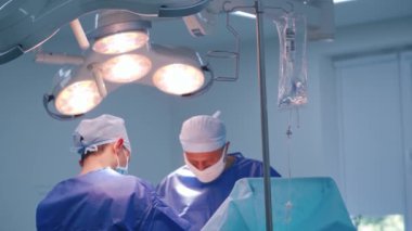 Tıbbi üniformalı cerrahlar ameliyat yapıyor. Modern klinikteki ameliyathanenin üzerinde parlak bir lamba. Sağlık hizmetleri kavramı.
