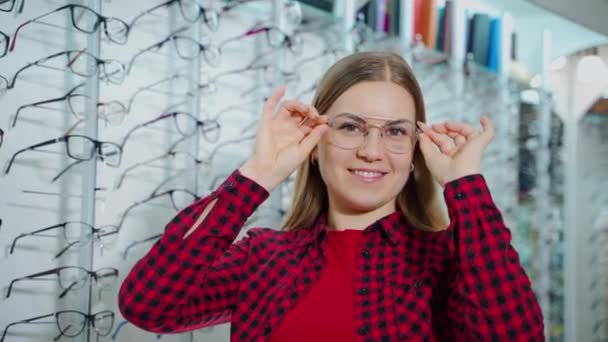 一个穿着时髦眼镜的快乐女人的画像 微笑的女买家选择新眼镜 并在光学商店摆出一副相机的样子 — 图库视频影像