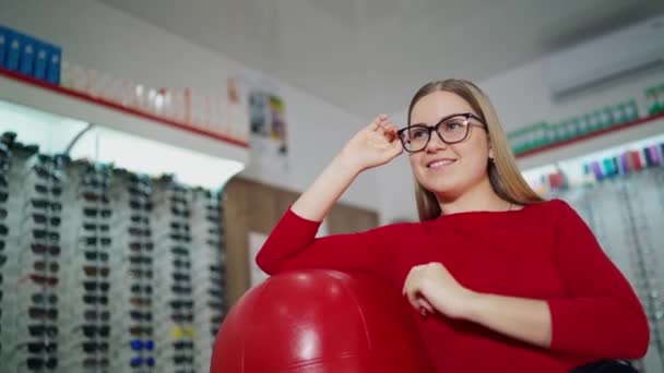 スタイリッシュな眼鏡で美しい女性 アームチェアに座り 光学店で新しいメガネを試してみる女性のお客様 アイウェアコンセプト — ストック動画