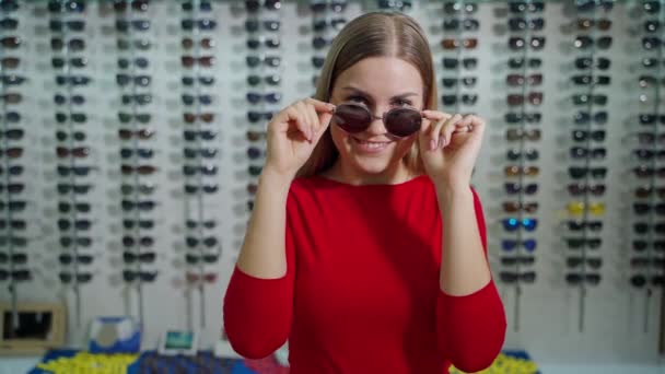 迷人的女孩选择太阳镜的肖像 在光学商店里 女买主穿着新的时髦眼镜 摆出一副相机的姿势 — 图库视频影像