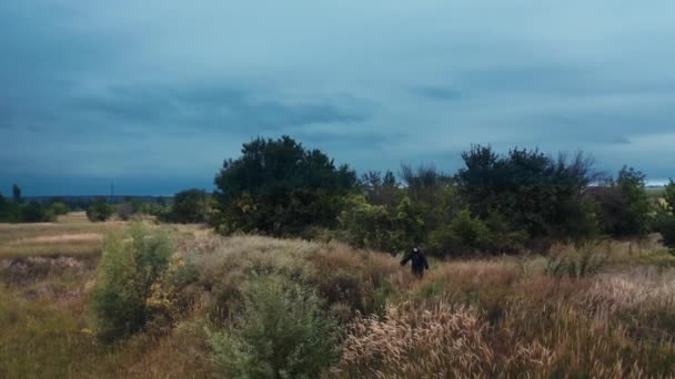 自然界中穿着黑色斗篷的神秘鬼魂 乌云密布的天空下 黑暗的身影屹立在田野上 可怕的死亡 恐怖概念 无人机视图 — 图库视频影像