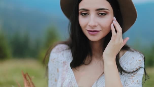 自然界中帽子中的深色头发的画像 迷人的年轻女子看着相机 在模糊的自然背景下微笑 — 图库视频影像