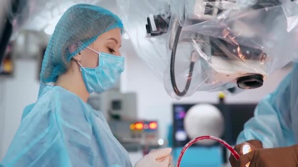 医用制服の女性アシスタントの側面 医療従事者は 診療所の近代的な機器の操作中に外科医を支援する — ストック動画