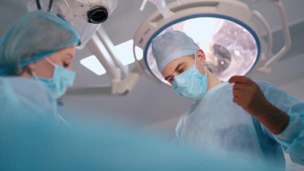 手术时戴口罩的医生的脸 外科医生和护士在现代医疗灯的背景下做手术 从下面看 — 图库视频影像