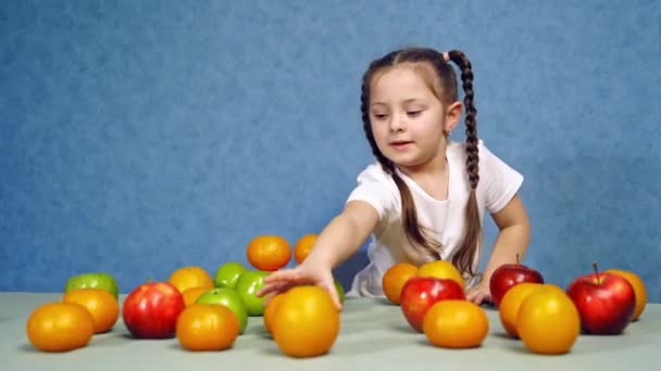 自宅で果物を持ったかわいい女の子 小さな子供がテーブルの上に新鮮な果物の塔を建てています 有機的な健康的な食べ物を持つ幸せな子供 — ストック動画
