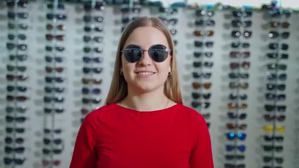 屋内でスタイリッシュなサングラスの女の子の肖像画 光学店の背景にファッショナブルな黒いメガネを着用する美しい若い女性 — ストック動画