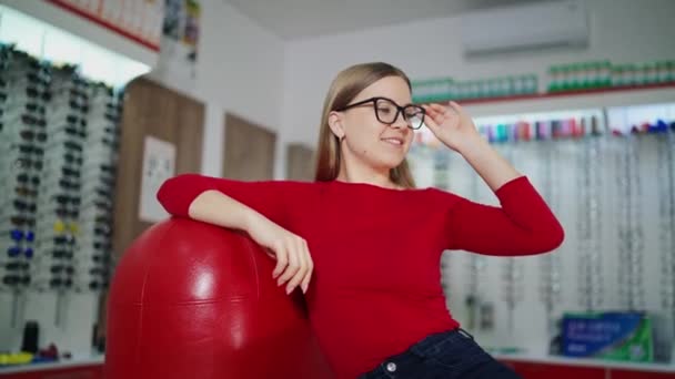 Urocza Dziewczyna Przymierza Nowe Okulary Optyce Piękna Kobieta Czerwieni Siedzi — Wideo stockowe
