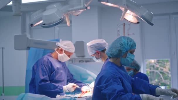 现代诊所的外科医生团队合作 身穿医疗制服的专业医生给病人做手术 在手术期间提供无菌器械的女助手 — 图库视频影像