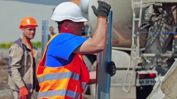 建筑工地安全帽工人在室外测量金属基座 建筑商为在地面上安装太阳能电池板奠定基础 — 图库视频影像
