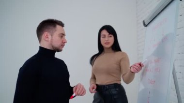 Genç bir kadın, erkeğe yeni projesini soruyor. Güzel dişi, iş ortağını dinler. Genç adam tahtaya bakarken kadına cevap verir..