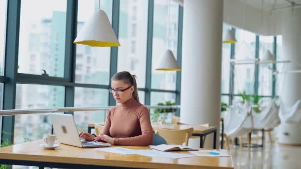 商务午餐时 一位漂亮的女商人穿着浅褐色的衬衫 坐在一家餐馆的大玻璃窗旁 在笔记本电脑上工作 — 图库视频影像