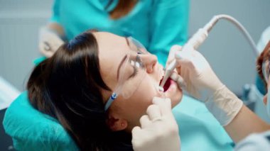 Stomatoloji kliniğinde ağzı açık bir kadın hasta. Profesyonel diş hekimi dişlerini tıbbi malzemelerle tedavi ediyor. Yakın plan..