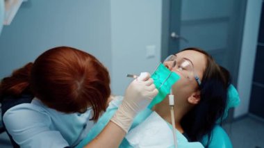 Diş tedavisi sırasında dişi ağrıyan bir kadın. Maskeli ve gözlüklü profesyonel kadın diş hekimi stomatoloji kliniğinde tıbbi aletler kullanıyor..