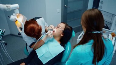 Profesyonel kadın stomatolog iş başında. Diş tedavisi sırasında dişçi koltuğunda oturan genç bir kadın. Dişçi dişçilikte modern tıbbi ekipman kullanır. Üst görünüm.