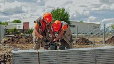 Güneş santrali inşaatı. Turuncu kasklı iki işçi güneş panelleri inşa etmek için aletler hazırlıyor. Mühendisler gelecekteki güneş enerjisi santrali için metal temeli kuruyorlar.