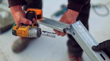 Mühendisler güneş panelleri için temel kuruyorlar. İşçinin elleri matkapla metal çerçeve bağlıyor. Yakın plan..