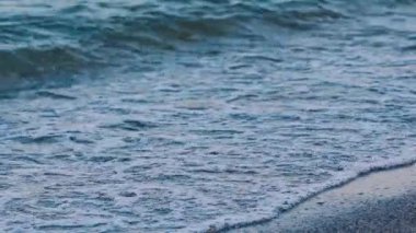 Deniz dalgaları kıyıda. Deniz suyunun muhteşem manzarası. Dalgalar beyaz köpük üreterek çakıl taşı plajına çarpar. Yavaş çekim.