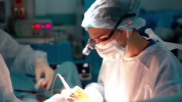 女性外科医が手術をしています 特別な壮大な眼鏡を用いた医療用制服の専門医は 現代の病院で医療機器を使用しています — ストック動画