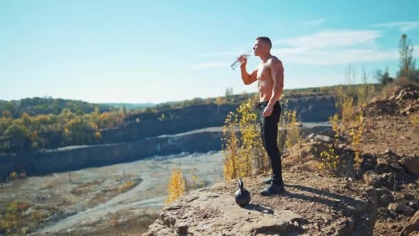 运动员正在室外用瓶子喝水 裸体健美者在经过大自然背景的艰苦训练后喝水 — 图库视频影像