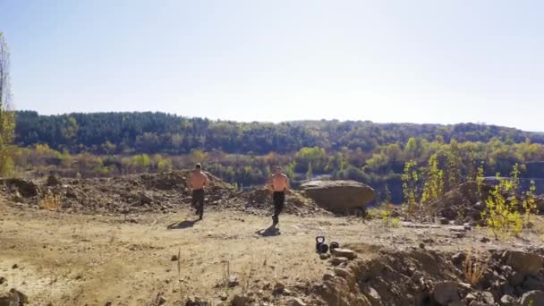 自然の中で2人のアスリートのトレーニングの裏側のビュー 丘の上に筋肉体のあるスポーティブなシャツレスの男性 エアリアルビュー — ストック動画
