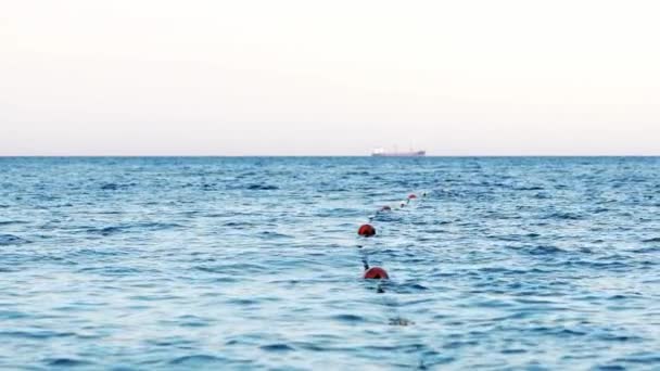 ロープのブイと青い海水の素晴らしい景色 海のマーカーが付いている安全な水泳ゾーン 遠くに浮かぶ大きな船 スローモーション — ストック動画