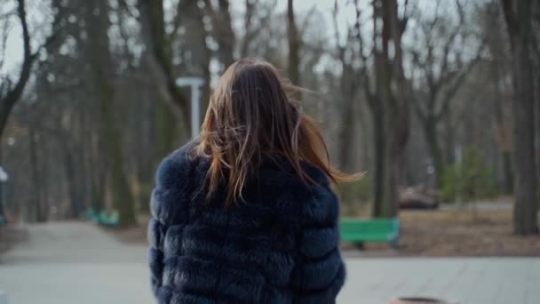 公園の毛皮のコートにいる若い女性 ある女の子がコーヒーのプラスチックカップでカメラに向かう様子 屋外でスタイリッシュな女性の肖像画 — ストック動画