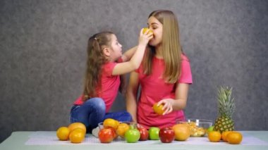 Mutlu küçük kız ve evde meyveleri olan annesi. Pembe tişörtlü anne ve kız mutfakta taze organik meyvelerle eğleniyorlar..