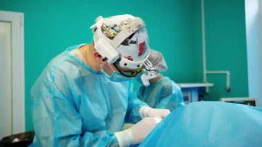 Cerrahi prosedür ameliyathanesi. Tıbbi üniforma ve cerrahi el feneri uzmanı ameliyat yapıyor. Asistanı klinikteki cerraha yardım ediyor..