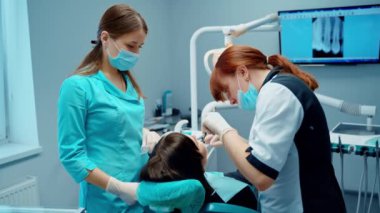 Asistanı olan dişçi hastanın dişlerini tedavi ediyor. Modern stomatoloji ofisinde dişçi prosedürü. Hasta ağız boşluğunda çalışan kadın dişçi..