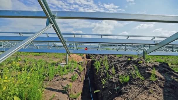 太陽光発電所を建設する 労働者は将来の太陽電池パネルのための金属の基盤の下で地面の電線をリードします クリーンエネルギーを得るための革新的な発電所 — ストック動画