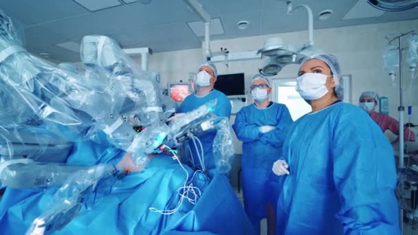外科手術を最小限に抑える未来ロボット 外科ロボットの近くのモニターを監視する制服とマスクの医師のチーム — ストック動画