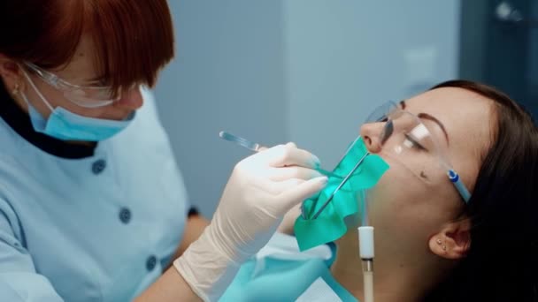 一个戴防护眼镜的病人的脸在牙椅上在牙科诊所治疗妇女牙齿的专业口腔科医生 口腔学概念 — 图库视频影像