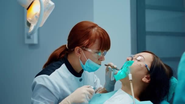 专业牙医治疗病人的牙齿 在现代口腔科办公室 坐在牙椅上张开嘴的妇女 护士把仪器交给医生 — 图库视频影像