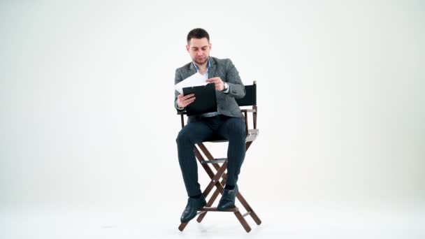 フォルダのあるエレガントな男 ビジネスマンが椅子に座って文書を読んでいる 多くの論文がハンサムな男の上にスタジオで飛んでいる — ストック動画
