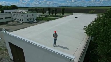 Doğanın arka planında çatıda duran erkek işçi. Gelecekteki güneş enerjisi santrali olan bir binada koruyucu miğfer takan mühendis. Kamera yükseliyor.