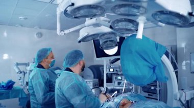 Klinikteki modern bir ameliyathanede ameliyat. Mavi üniformalı doktorlar, profesyonel ekipman kullanan bir hastayı ameliyat ediyorlar..