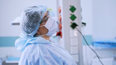 Ameliyathanede maskeli bir hemşirenin yan görüntüsü. Klinikte salgın sırasında koruyucu giysili, gözlüklü ve maskeli bir tıbbi asistan. Coronavirus, korona konsepti.