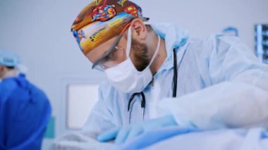 Hastanede maskeli ve gözlüklü profesyonel bir doktor var. Koruyucu üniformalı erkek cerrah ameliyathanede çalışıyor..