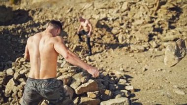 Erkekler güneşli bir günde taş atarak egzersiz yaparlar. İki üstsüz sporcu kayalıklarda antrenman yapıyor. Yavaş çekim.
