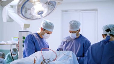 Cerrahların ekip çalışması ameliyathanede. Üniformalı ve maskeli tıp uzmanları hastanedeki modern tıbbi lamba altında ameliyat yapıyorlar..