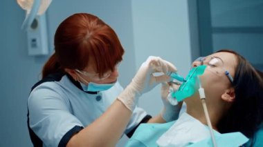 Diş hekimi klinikte kadınların dişlerini tedavi ediyor. Profesyonel dişçi diş muayenehanesindeki bir hastaya ağız boşluğuna enjeksiyon yapıyor..