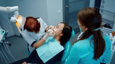 Kadın dişçi ve dişçi koltuğunda bir müşteri. Profesyonel stomatolog ve asistanı dişçi muayenehanesinde hastanın dişini tedavi ediyor. Üst görünüm.